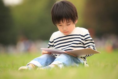 Çimenlerde oturup kitap okuyan tatlı çocuk.