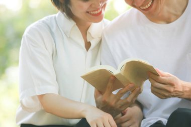 Asyalı çift yeşil çayır üzerine kitap okuyor