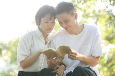 Asyalı çift yeşil çayır üzerine kitap okuyor