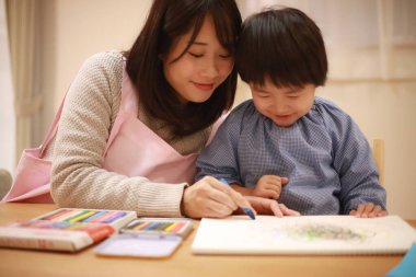 Annesiyle birlikte çizen yakışıklı Asyalı çocuk.