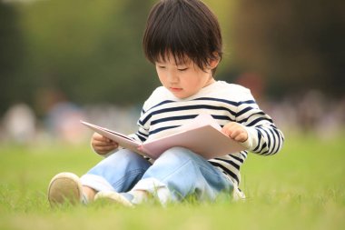 Çimenlerde oturup kitap okuyan tatlı çocuk.