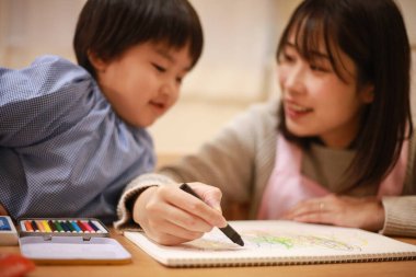 Annesiyle birlikte çizen yakışıklı Asyalı çocuk.