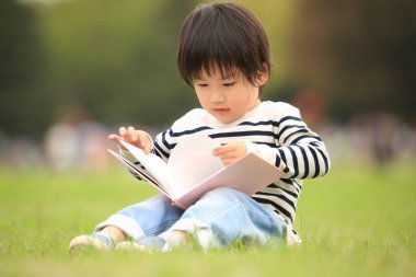 Çimenlerde oturup kitap okuyan tatlı çocuk.