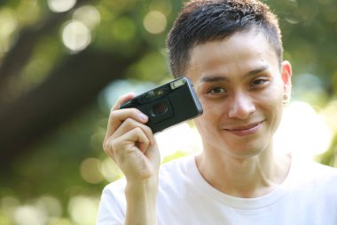 Genç ve yakışıklı bir adam parkta fotoğraf makinesi çekiyor.