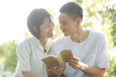 Asyalı çift yeşil çayır üzerine kitap okuyor