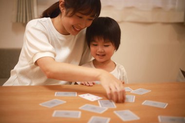 Asyalı anne ve oğlu birlikte kağıt oynuyorlar. 