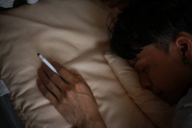 Asyalı bir adam yanan sigarayla yatakta uyuyor. 