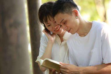 Asyalı çift yeşil çayır üzerine kitap okuyor