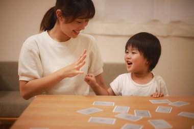 Asyalı anne ve oğlu birlikte kağıt oynuyorlar. 