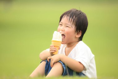 Küçük çocuk parkta dondurma yiyor.
