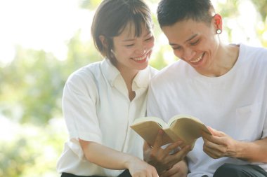 Asyalı çift yeşil çayır üzerine kitap okuyor