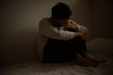 Genç üzgün adam, karanlık odada yerde oturuyor. 