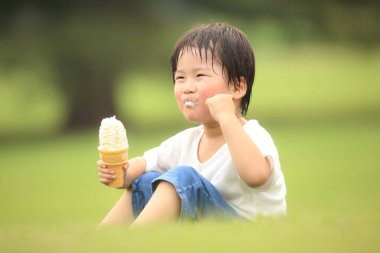 Küçük çocuk parkta dondurma yiyor.