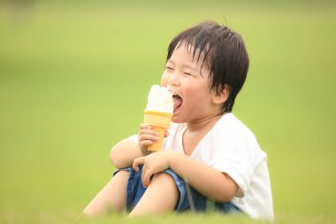 Küçük çocuk parkta dondurma yiyor.