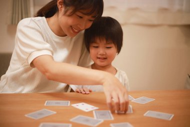 Asyalı anne ve oğlu birlikte kağıt oynuyorlar. 
