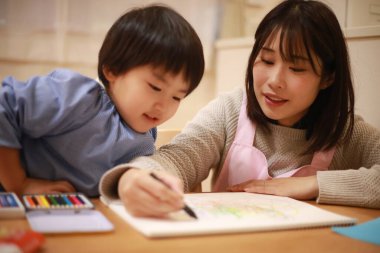 Annesiyle birlikte çizen yakışıklı Asyalı çocuk.