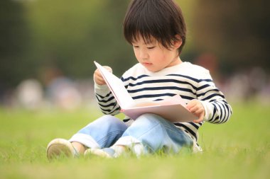 Çimenlerde oturup kitap okuyan tatlı çocuk.