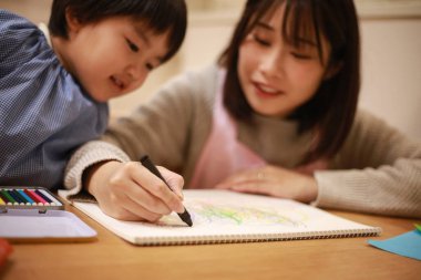 Annesiyle birlikte çizen yakışıklı Asyalı çocuk.