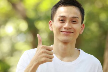 Başparmağını gösteren ve kameraya gülümseyen genç bir adamın portresi.