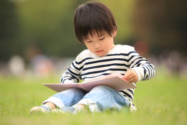 Çimenlerde oturup kitap okuyan tatlı çocuk.