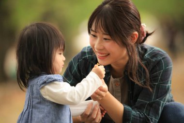 Genç anne ve kızı parkta küçük bir kızla oynuyorlar.