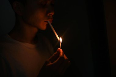 Genç Asyalı adam sigara yakıyor.