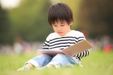 Çimenlerde oturup kitap okuyan tatlı çocuk.