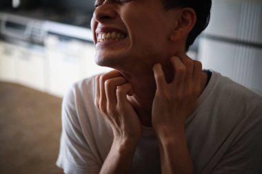 Asyalı genç adamın boğazı ağrıyor ve boynuna dokunuyor.