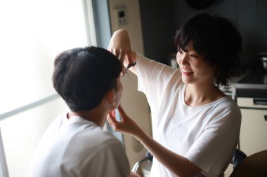 Genç Asyalı kadın evde erkek arkadaşının saçını kesiyor. 