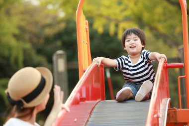 Genç anne ve sevimli mutlu küçük oğul parkta birlikte oynuyorlar.