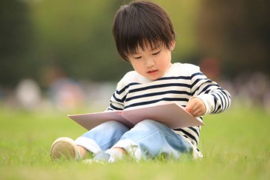 Çimenlerde oturup kitap okuyan tatlı çocuk.