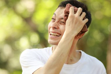 Stresli Asyalı adam terini havluyla temizliyor.