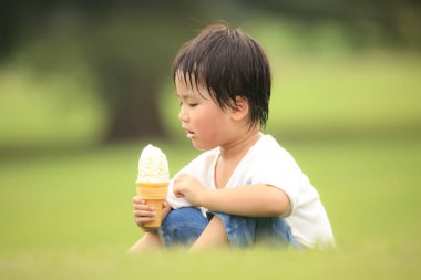 Küçük çocuk parkta dondurma yiyor.