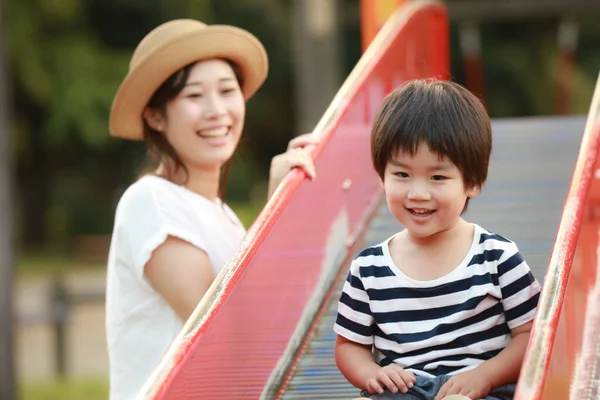 公園の遊び場で一緒に遊んでいる若い母親と愛らしい幸せな小さな息子 — ストック写真