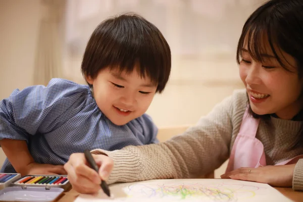 Annesiyle birlikte çizen yakışıklı Asyalı çocuk.