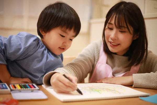 Annesiyle birlikte çizen yakışıklı Asyalı çocuk.