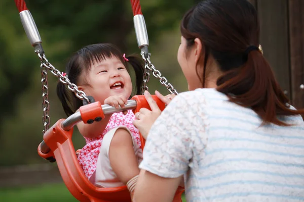 Genç anne küçük kızıyla oyun parkında oynuyor.
