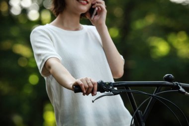 Bisikletli Asyalı kız elinde akıllı telefon tutuyor. 