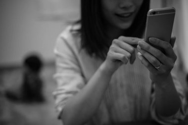 Genç Asyalı anne akıllı telefon kullanıyor, çocuk arka planda.