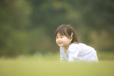 Parktaki çimlerin üzerindeki küçük Japon kızın portresi.