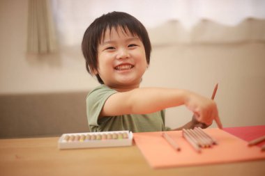 Küçük çocuk evde kalemlerle oynuyor.