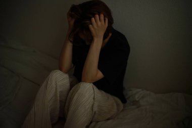 Odadaki yatakta pijamalı üzgün bir kadın oturuyor.