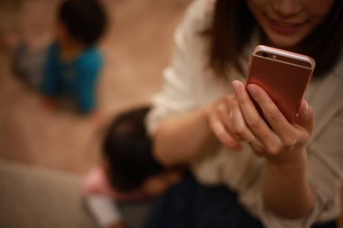 Genç Asyalı anne akıllı telefon kullanıyor, çocuklar arka planda.