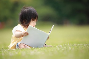 Yeşil parkta kitap okuyan sevimli küçük kız