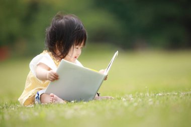 Yeşil parkta kitap okuyan sevimli küçük kız