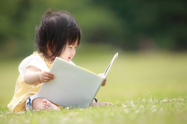 Yeşil parkta kitap okuyan sevimli küçük kız