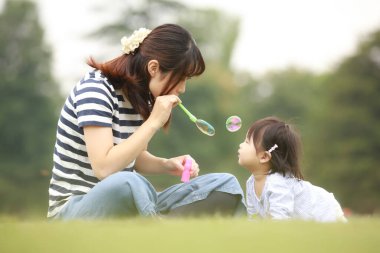 Mutlu anne ve kız sabun köpüğüyle çimenlerde oynuyorlar. 