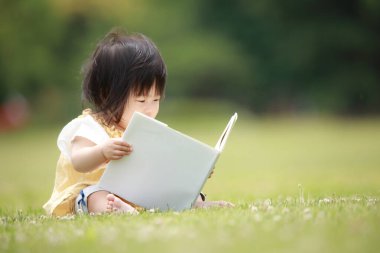 Yeşil parkta kitap okuyan sevimli küçük kız