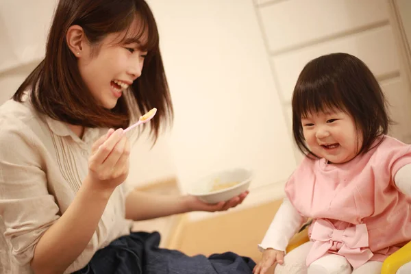 若いアジア系の母親が台所で娘を養い — ストック写真
