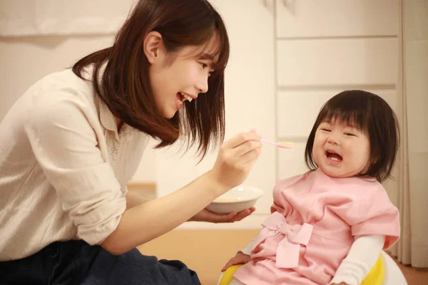 若いアジア系の母親が台所で娘を養い — ストック写真